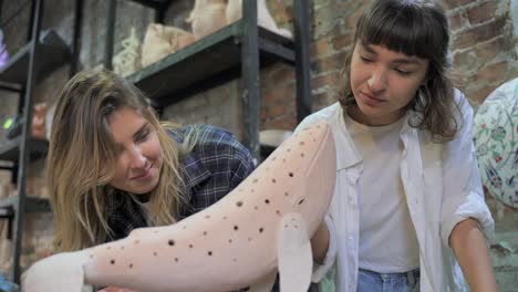 two women inspecting a clay whale sculpture in an art studio