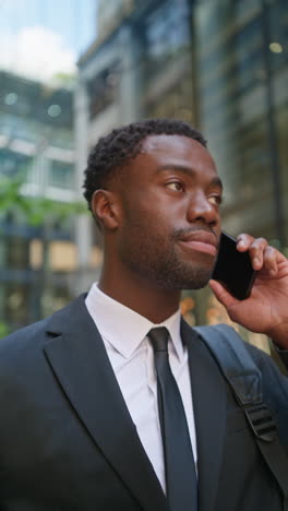 vertical video shot of serious young businessman wearing suit talking on mobile phone standing outside offices in the financial district of the city of london uk shot in real time 2