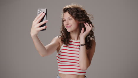 brunette girl fixes hair and takes selfie with phone, studio shot