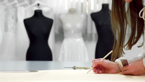 beautiful girl fashion designer draws on the paper templates for cutting out fabric on the mannequins dressed in wedding dresses. manufacturer of wedding dresses.