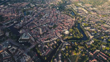 Vista-Aérea-Del-Amanecer-De-Amsterdam-Con-Edificios-Históricos,-Canales-Y-Espacios-Verdes-Urbanos-Vivos