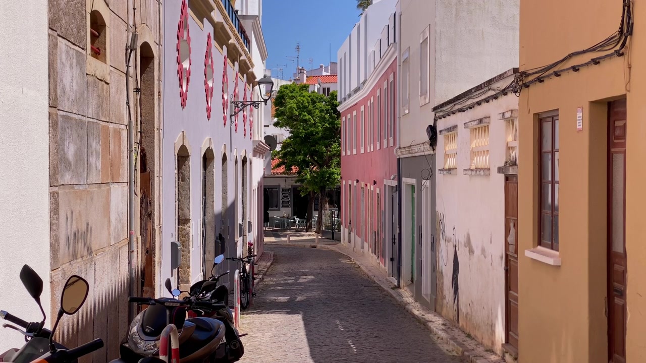 Gade i den gamle bydel i Lagos, Portugal, der viser traditionel arkitektur og en livlig atmosfære med parkerede scootere