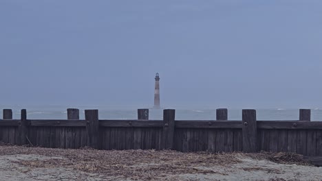 Misterioso-Rompeolas-De-Madera-Y-Leer-Faro-Rayado-En-Un-Fondo-Lejano-En-El-Atardecer-Nublado