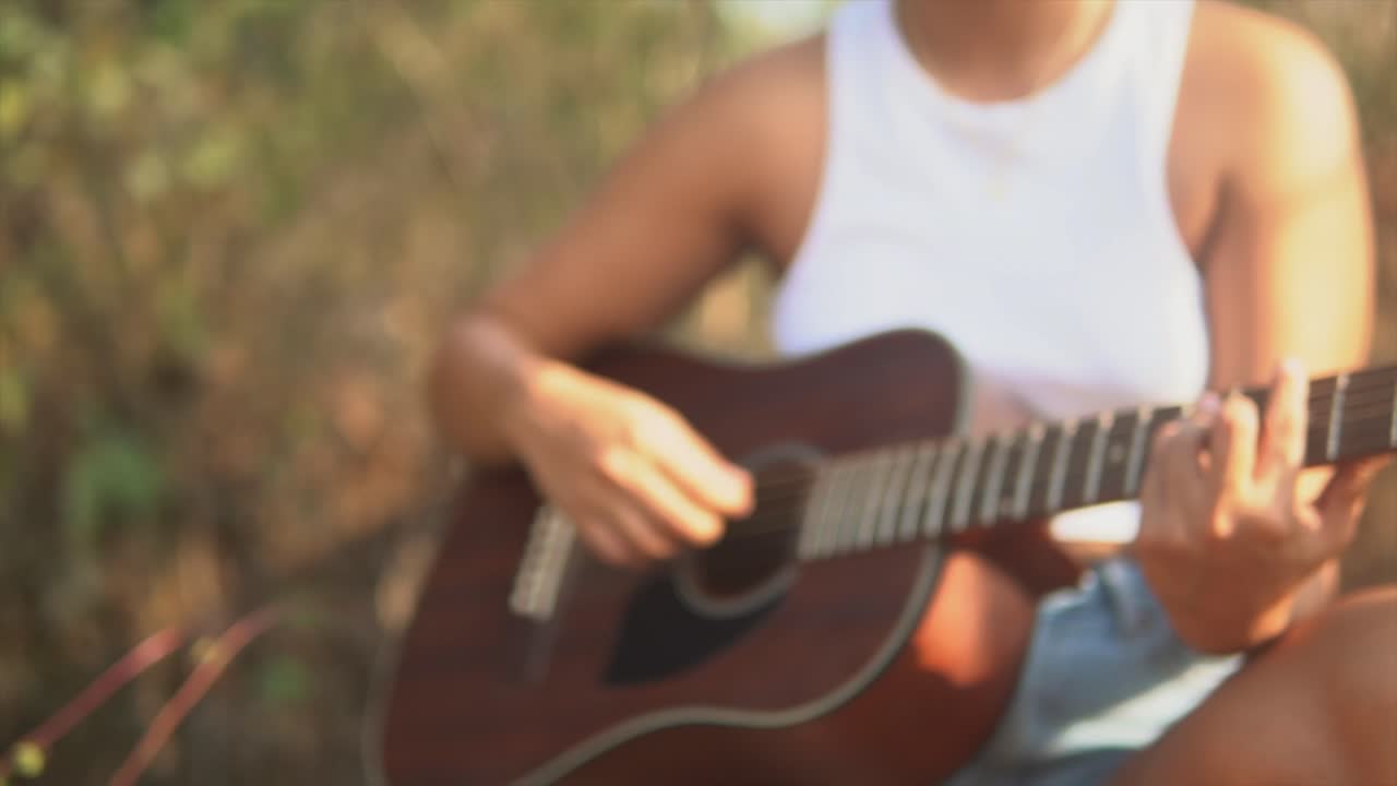 mujer sentada rasgueando una guitarra en la naturaleza closeup borrosa