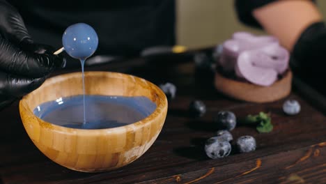 pastry chef is dips a candy in caramel for topping a blueberry cake, close-up