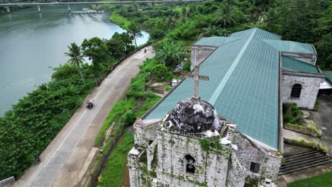 cinematic, establishing aerial view of local, riverside catholic church alongside tricycles driving on road and lush rainforests