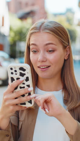 young woman using smartphone scrolling typing text messages in mobile navigator app on street