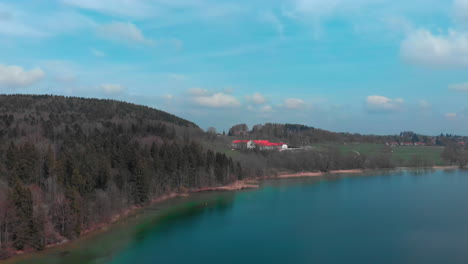 Aerial-pan-while-ascending,-showing-Gut-Kaltenbrunn-and-the-crystal-clear-water-of-the-Tegernsee-in-Bavaria