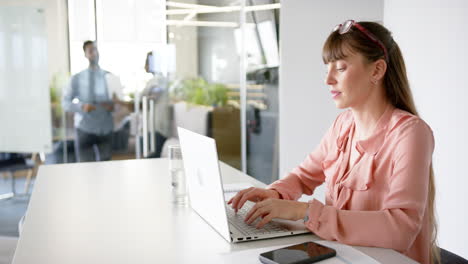 typing on laptop, woman working in modern office with smartphone and glass of water, copy space