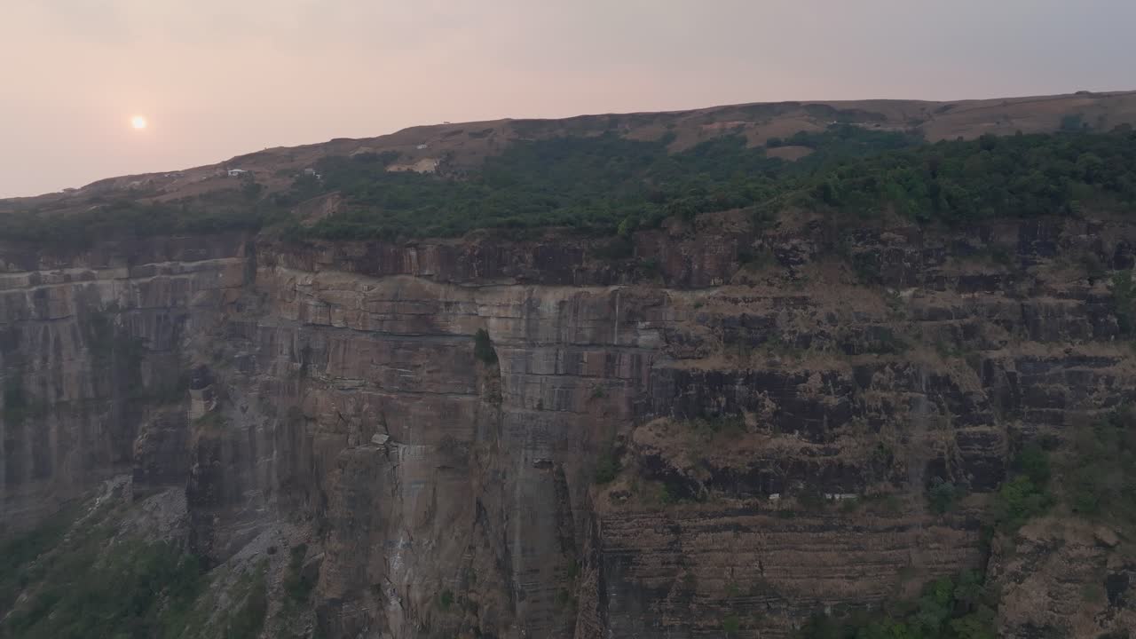 Cherrapunji, Meghalaya, India — scogliere di arenaria stratificate si ergono sopra la vegetazione verde durante il tramonto della stagione secca. Il cielo crepuscolare rosa e viola sfuma sul paesaggio dell'altopiano.