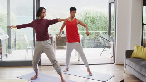 happy diverse male couple doing yoga, stretching in living room