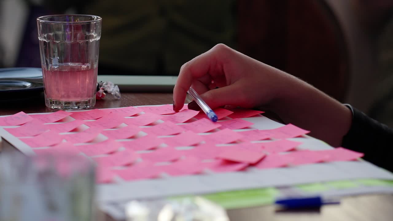 A hand placing notes on a table during a brainstorming session with a drink nearby