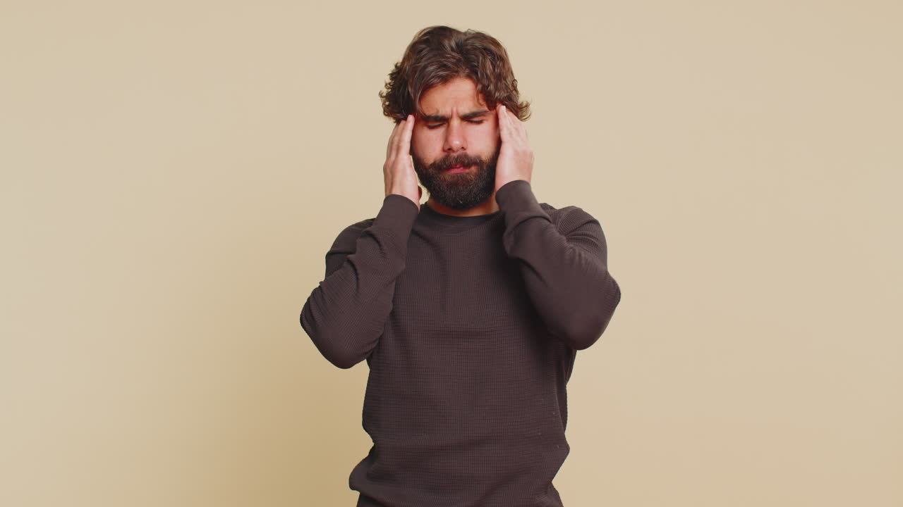 Lebanese bearded man in long sleeves rubbing temples to cure headache problem on beige background