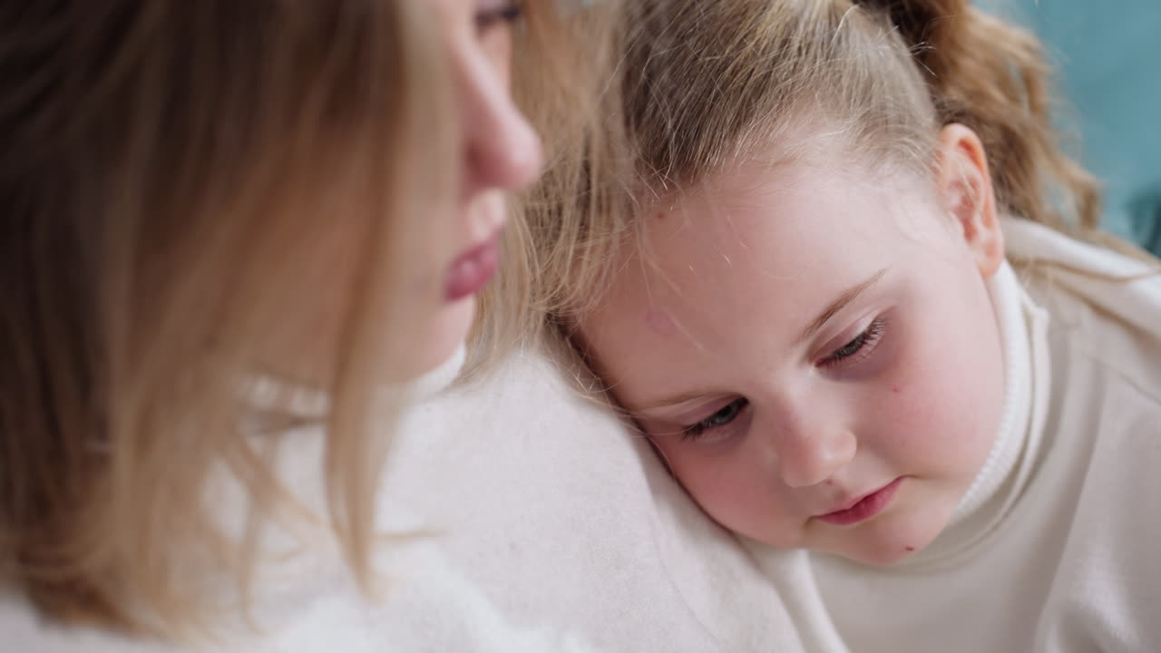 Little girl rests head on woman shoulder with tender and thoughtful expression, wearing white turtleneck, showing calm emotion and quiet bonding moment in warm family atmosphere