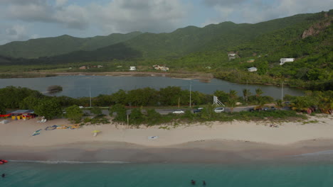 Aerial-tracking-view-4wd-vehicle-drive-on-Antigua-and-Bermuda-coast-with-blue-turquoise-waters-and-sandy-beach