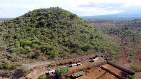 aerial of fill covered in green trees and bushes with small buildings at foot of hill in rural kenya