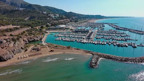 Puerto-Deportivo-Ginesta-Lleno-De-Barcos-Con-Playa-Y-Rompeolas,-Cerca-De-Barcelona,-España,-Día-Soleado,-Vista-Aérea