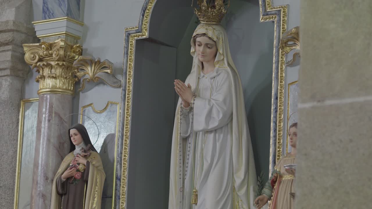 Socha Panny Marie modlící se uvnitř zdobeného oltáře katolického kostela s náboženskými sochami.