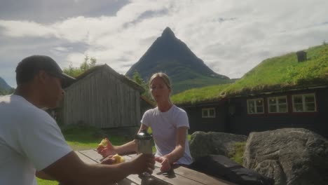 couple resting and eating at a picnic table in a scenic norwegian mountain landscape with traditional houses