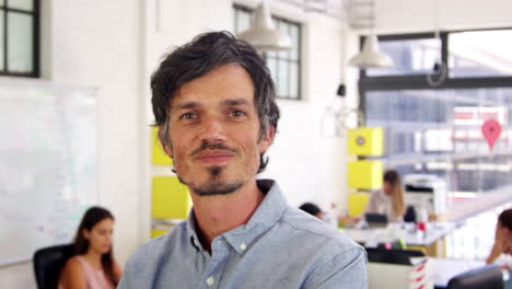 Mid-adult-white-man-in-office-walks-into-focus-and-smiles