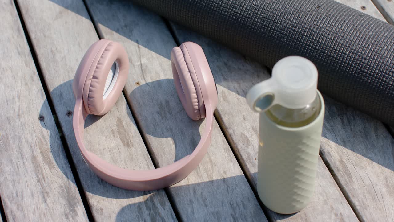 La fotocamera inizia a registrare cuffie rosa pallido e borraccia poggiata su un tappetino da yoga grigio per fare esercizio