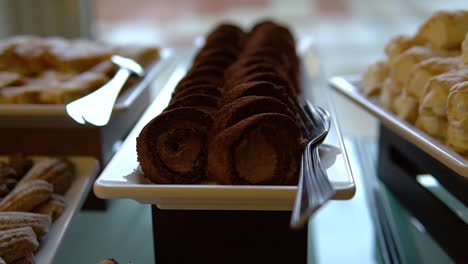 chocolate swiss roll filled with cream on a white tray with other sweets nearby