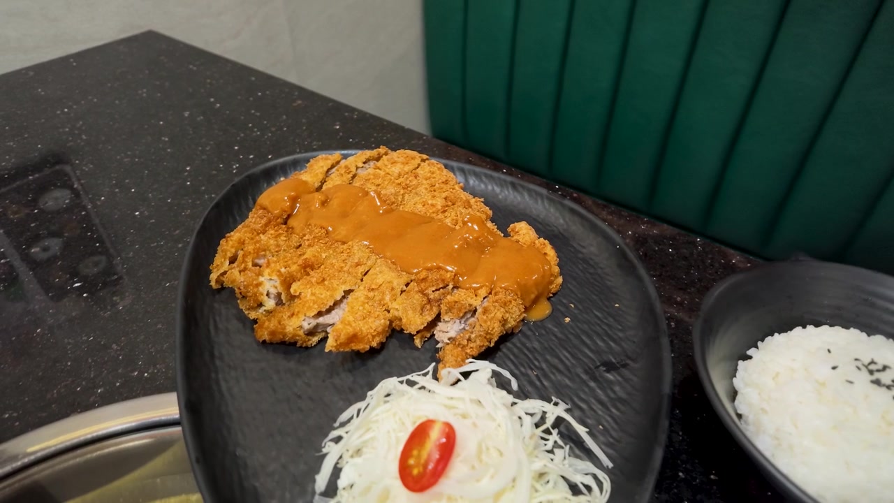 Foto close-up potongan daging babi dilapisi tepung roti yang disajikan dengan nasi dan salad di sebuah restoran.