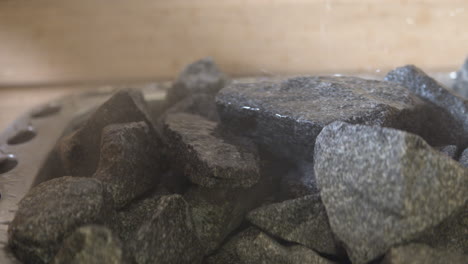 Closeup-truck-shot-of-some-hot-stone-inside-a-wooden-sauna,-water-being-poured-creating-steam