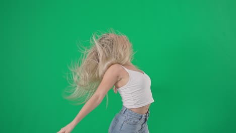 professional cheerful female dancer with long hair is spinning and dancing on an angry background, smiling and looking at camera on green background