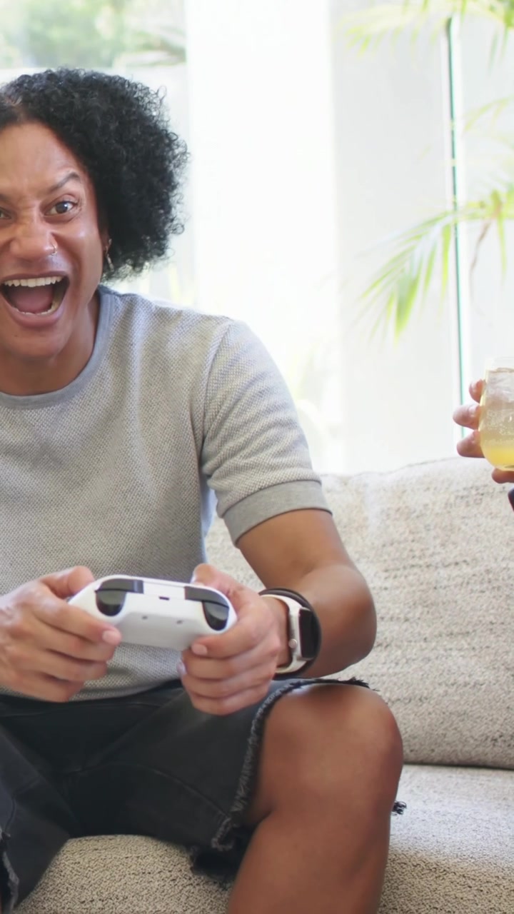 Man pressing white controller, woman holding drink watching, animated HUD showing score for gaming