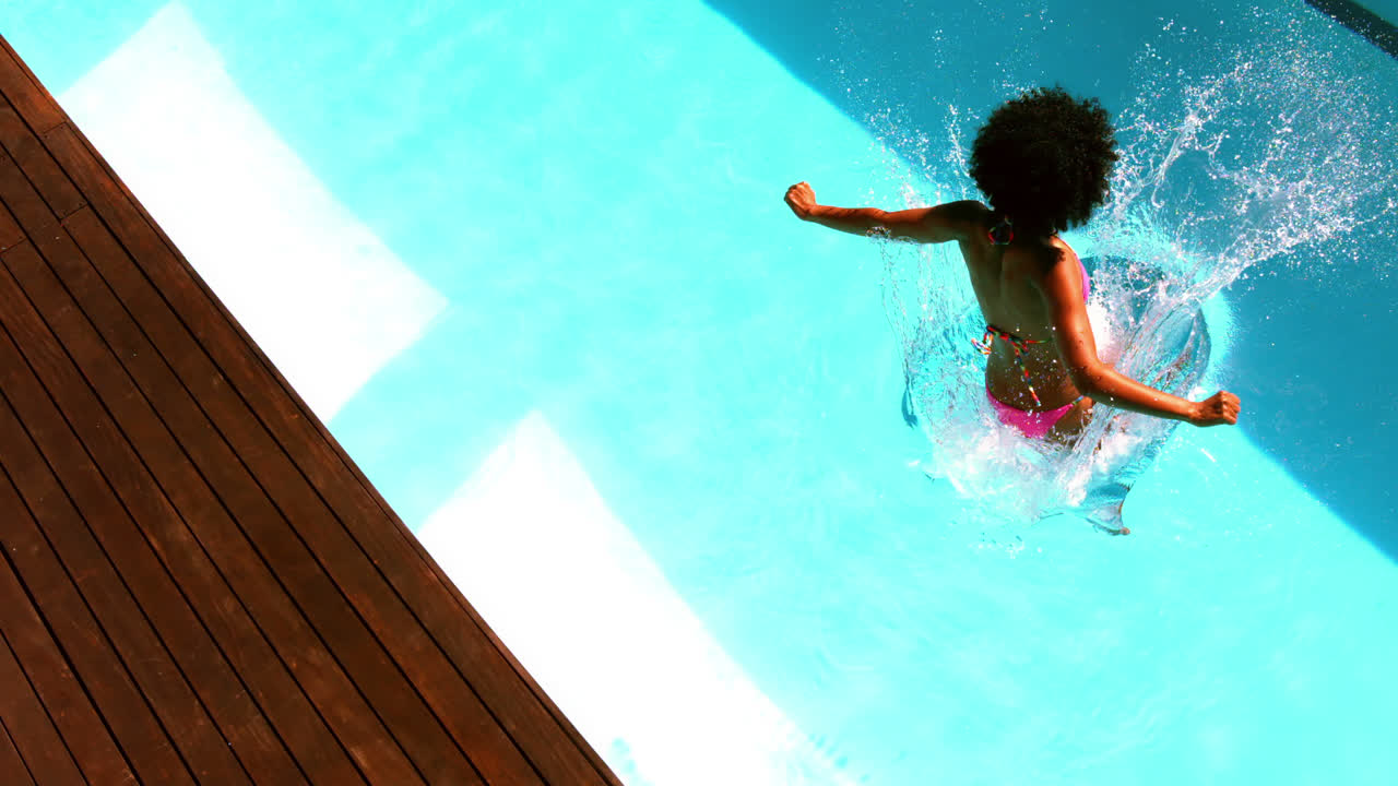 Frau im pinkfarbenen Bikini springt in einen Swimmingpool.