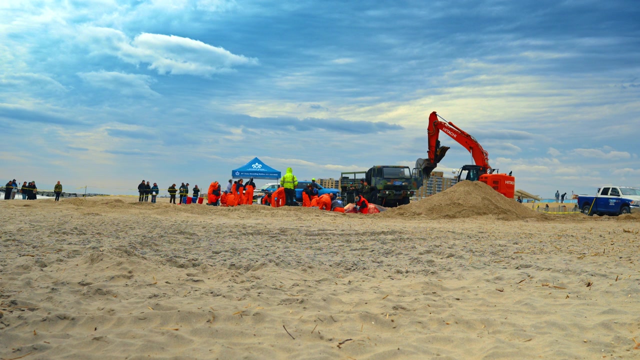 New York, USA, 1 aprile 2026: Vista panoramica di necroscopia di balena e operazione di sepoltura sulla spiaggia. Inquadratura grandangolare di un team di ricerca, escavatore e camion che gestiscono una balena morta su una spiaggia sabbiosa di New York.