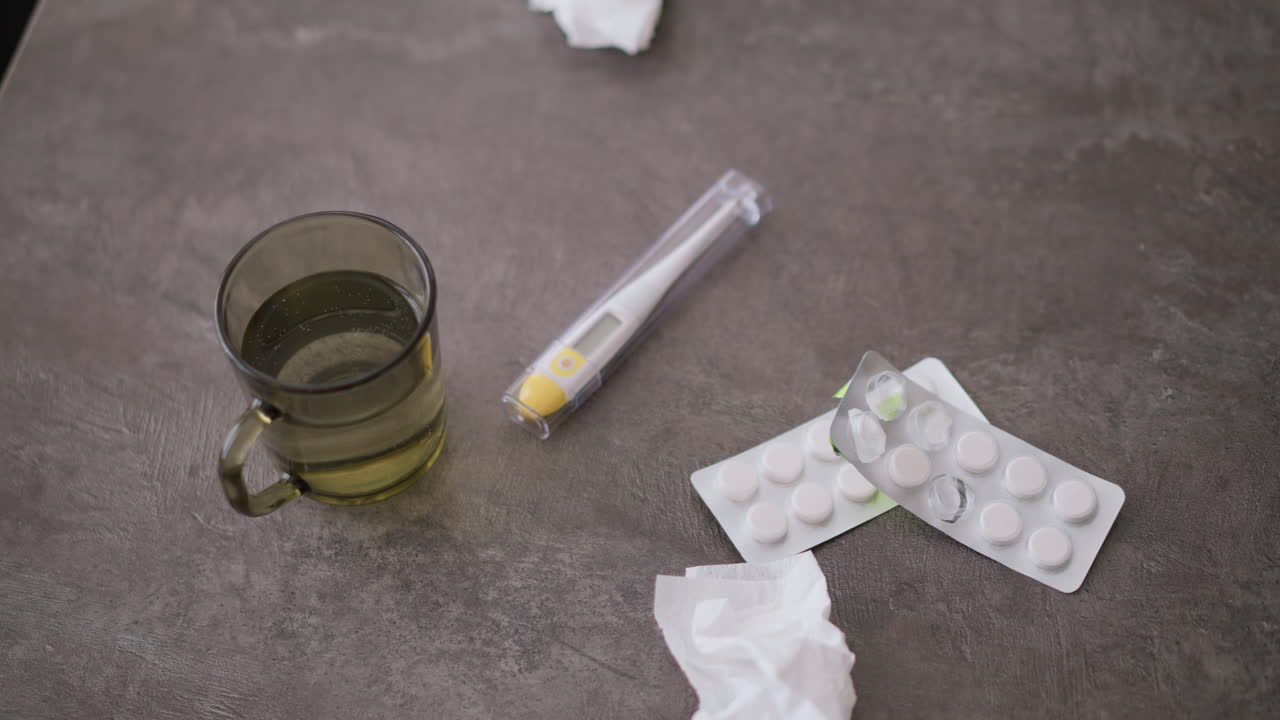 Close-up of medical items including used tissue, medication, and glass of water on table, showing signs of illness recovery with health-related items, reflecting treatment and wellness