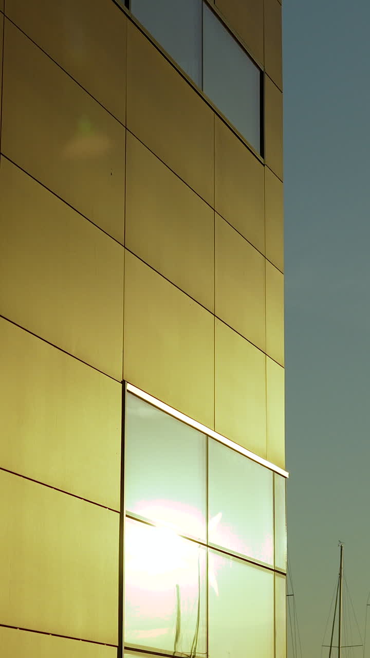 Uma tomada vertical em ângulo baixo de um edifício moderno com painéis metálicos dourados e janelas de vidro refletindo o sol brilhante do entardecer.