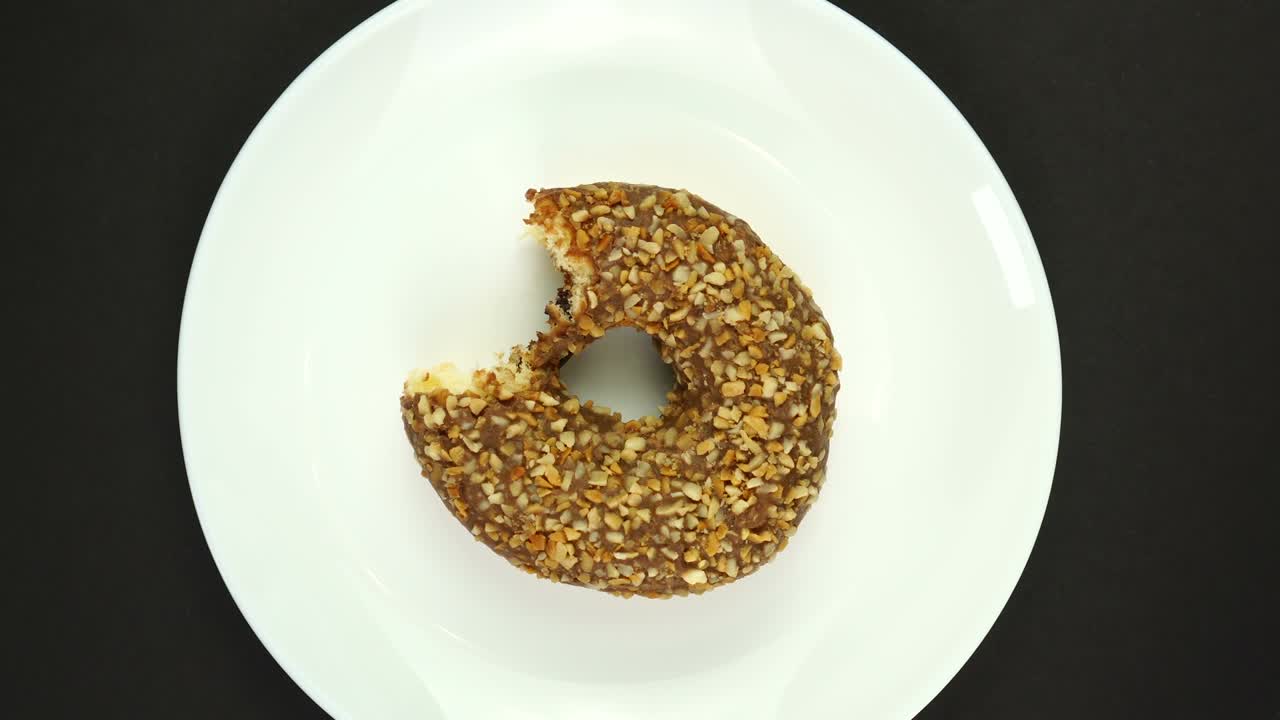 rosquilla mordida con glaseado de chocolate lechoso girando sobre un fondo negro.