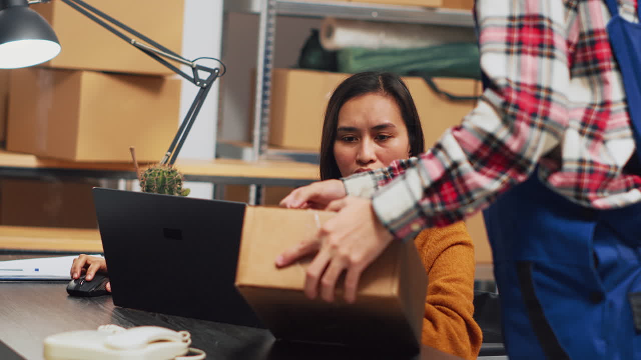 Woman working on laptop in warehouse with boxes
