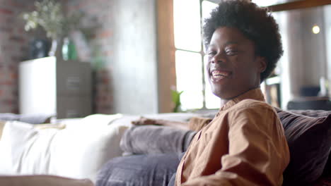 Portrait-of-happy-african-american-man-with-afro-sitting-on-sofa-at-home,-slow-motion