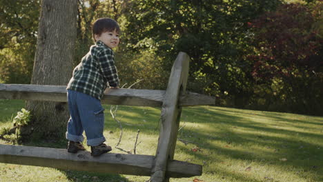 Agile-Asian-boy-2-years-old-climbed-the-fence,-has-a-good-time-on-a-walk-in-the-countryside