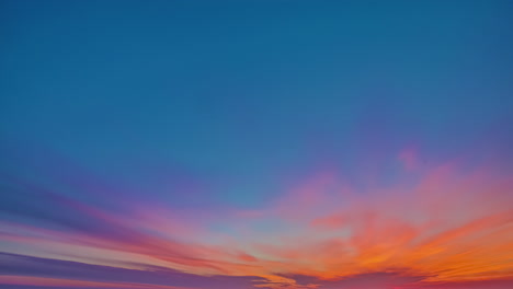 a bright blue sky in which deep orange colored clouds pass at a sunrise