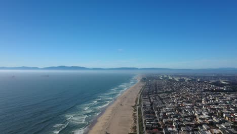 Vista-Aérea-De-La-Playa-De-Manhattan-En-California-Bajo-Un-Cielo-Azul-Claro-Con-Casas-Costeras-A-Lo-Largo-Del-Tramo-Arenoso