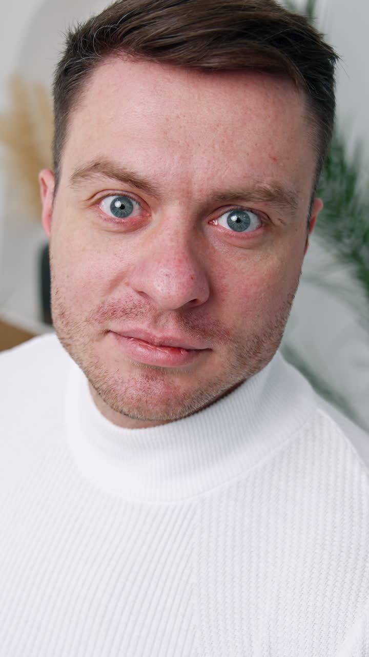 Caucasian male wearing white sweater standing near the camera. Cropped image of a man in the room. Close up. Vertical video