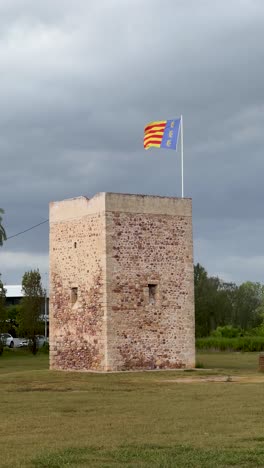 vertical footage of the valencian flag waving over a defensive medieval tower with stormy clouds in the background