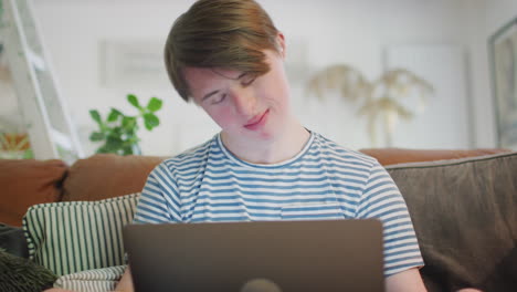 young downs syndrome man sitting on sofa watching laptop at home and dancing