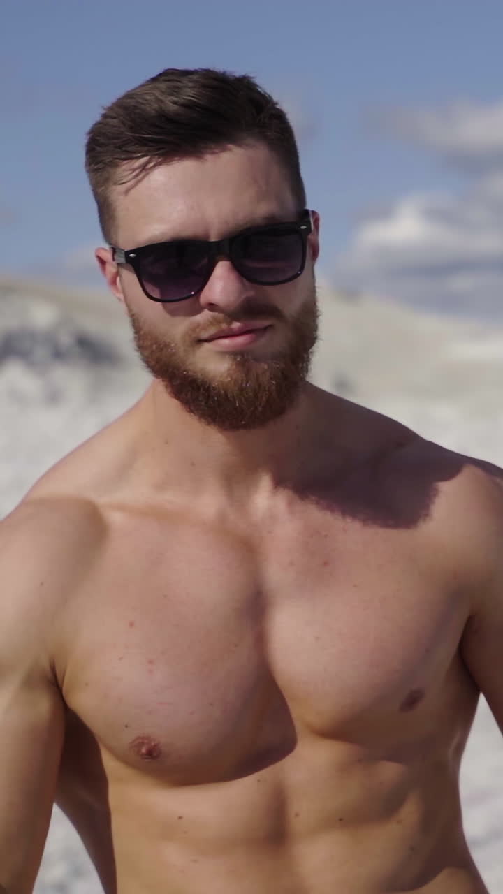 Muscular sportsman outdoors. Handsome shirtless man showing his arm biceps while standing on white canyon on black car background in summer day. Close-up. Vertical video