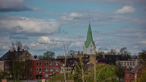 Timelapse-footage-of-Dobele,-Latvia,-focusing-on-a-church-tower-and-private-residences-as-clouds-periodically-pass-over-the-sun