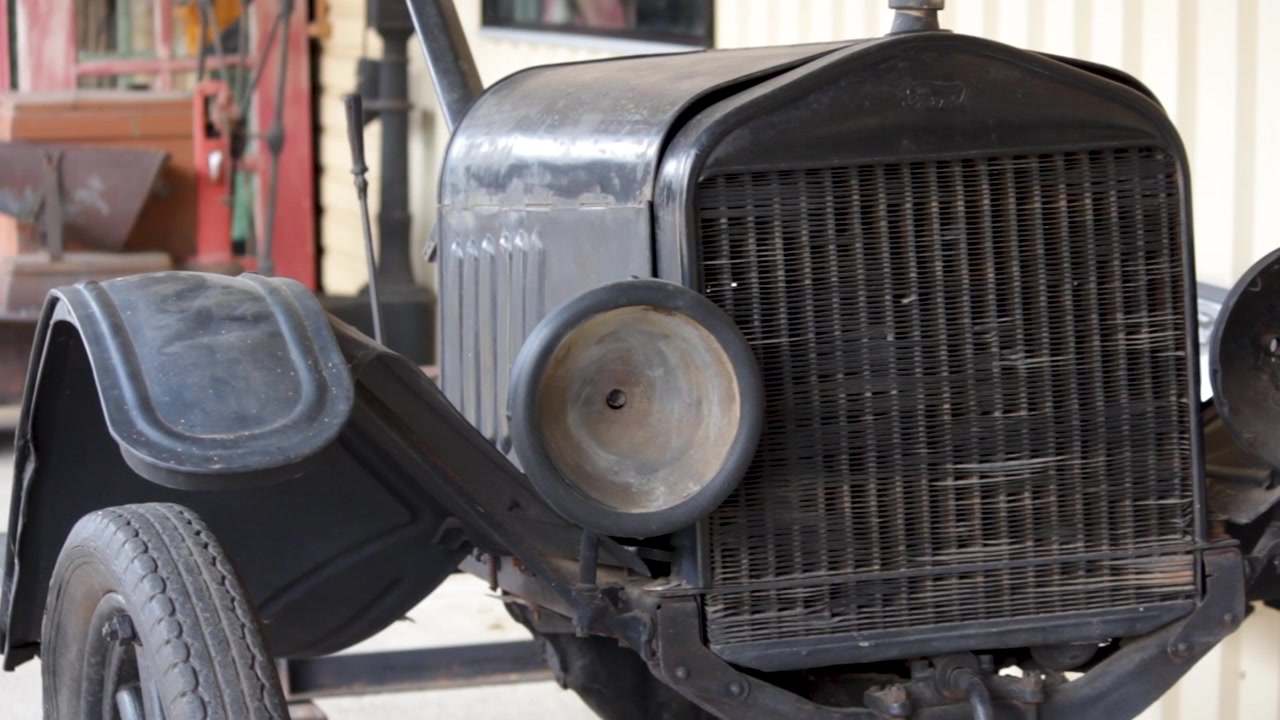 Weathered vintage car front end with one missing headlight and exposed grille.
