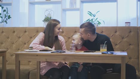 father-and-kid-look-at-mom-and-talk-sitting-in-restaurant