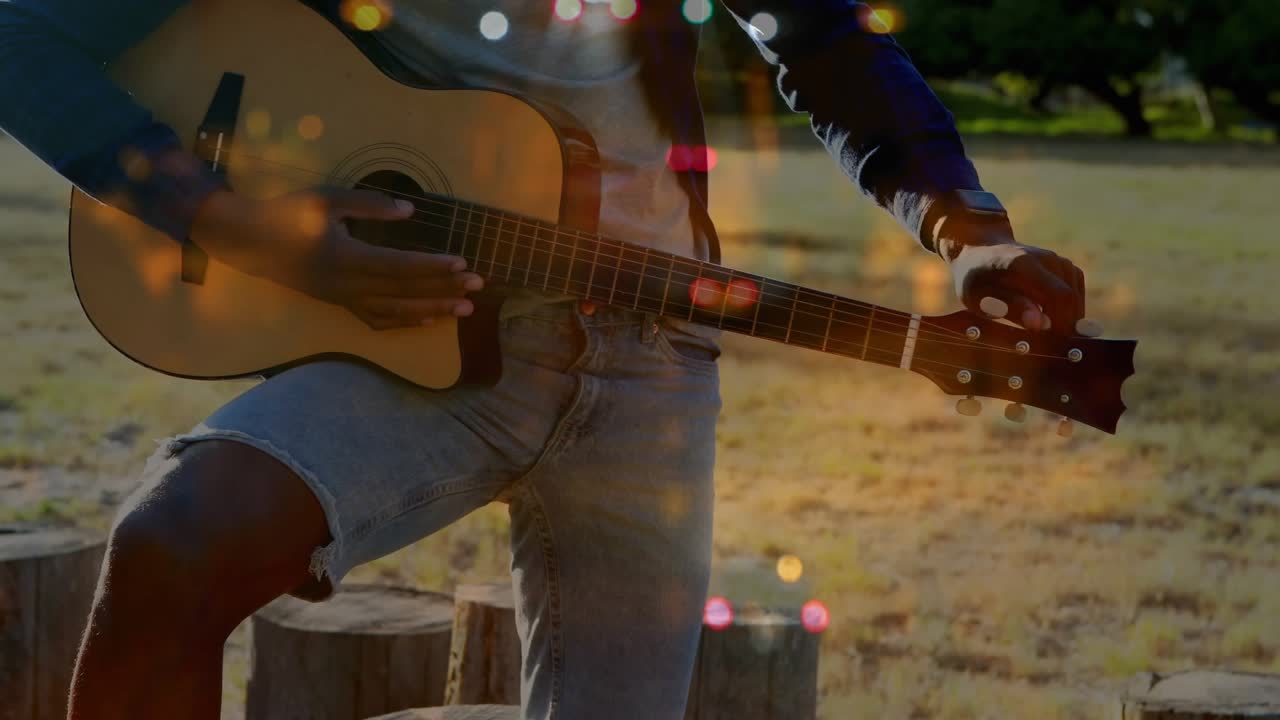 Male musician turning peg, strumming chords in park preparing music with layered bokeh overlay