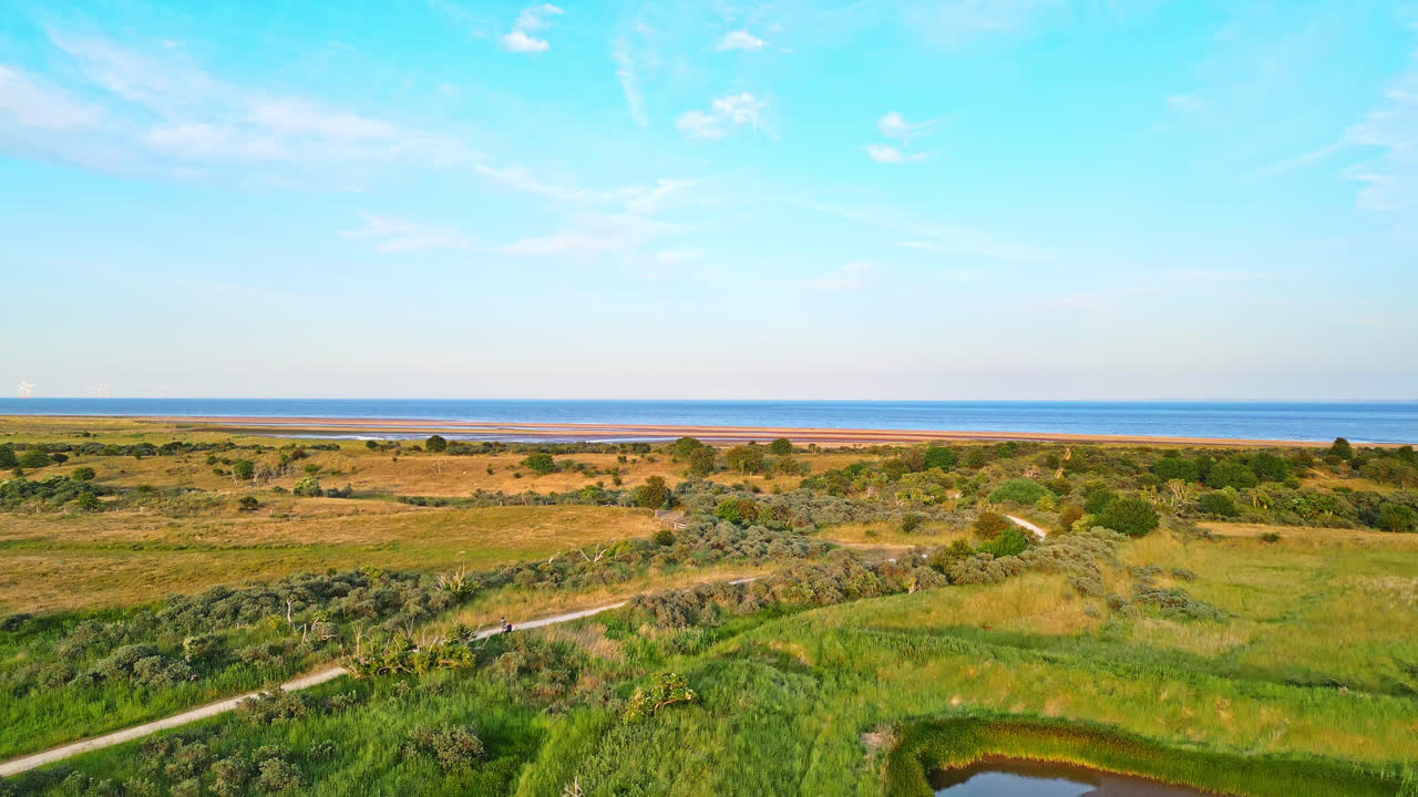 황금 시간의 해안 풍경의 이 ⁇ 한 매력을 드론으로 찍은 숨 막히는 영상으로 발견하십시오. 강 입구, 모래 언덕, 바다, 습지