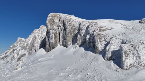 Snow-covered-Strungile-Mari-Peak-under-a-clear-blue-sky-in-Bucegi-Mountains,-daytime